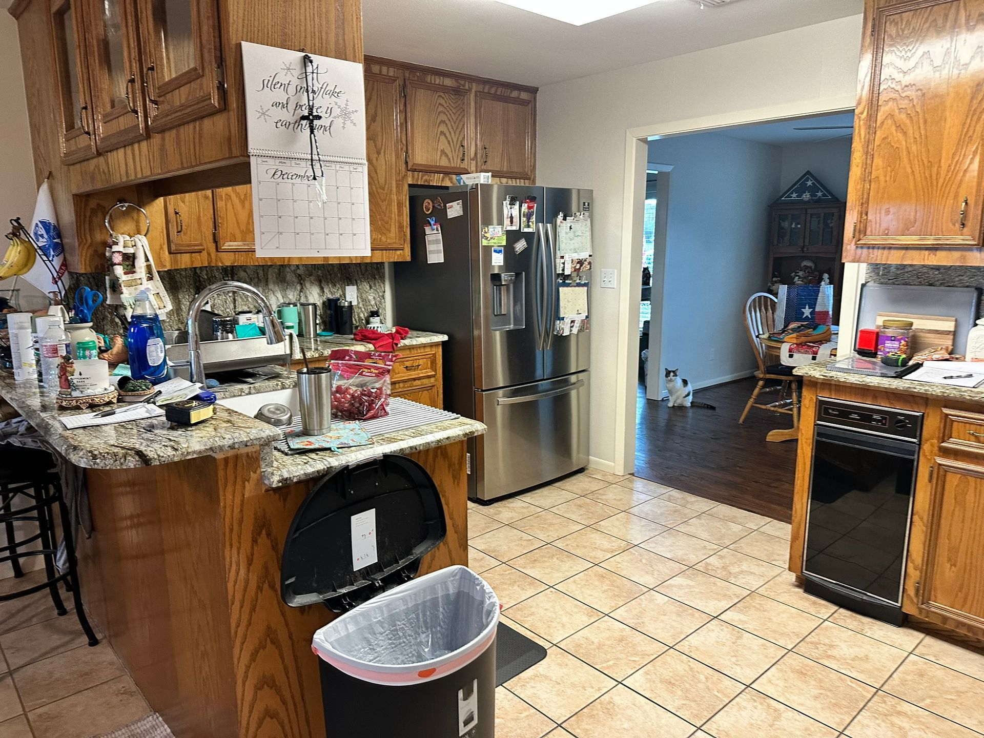 A kitchen with a stainless steel refrigerator and a trash can