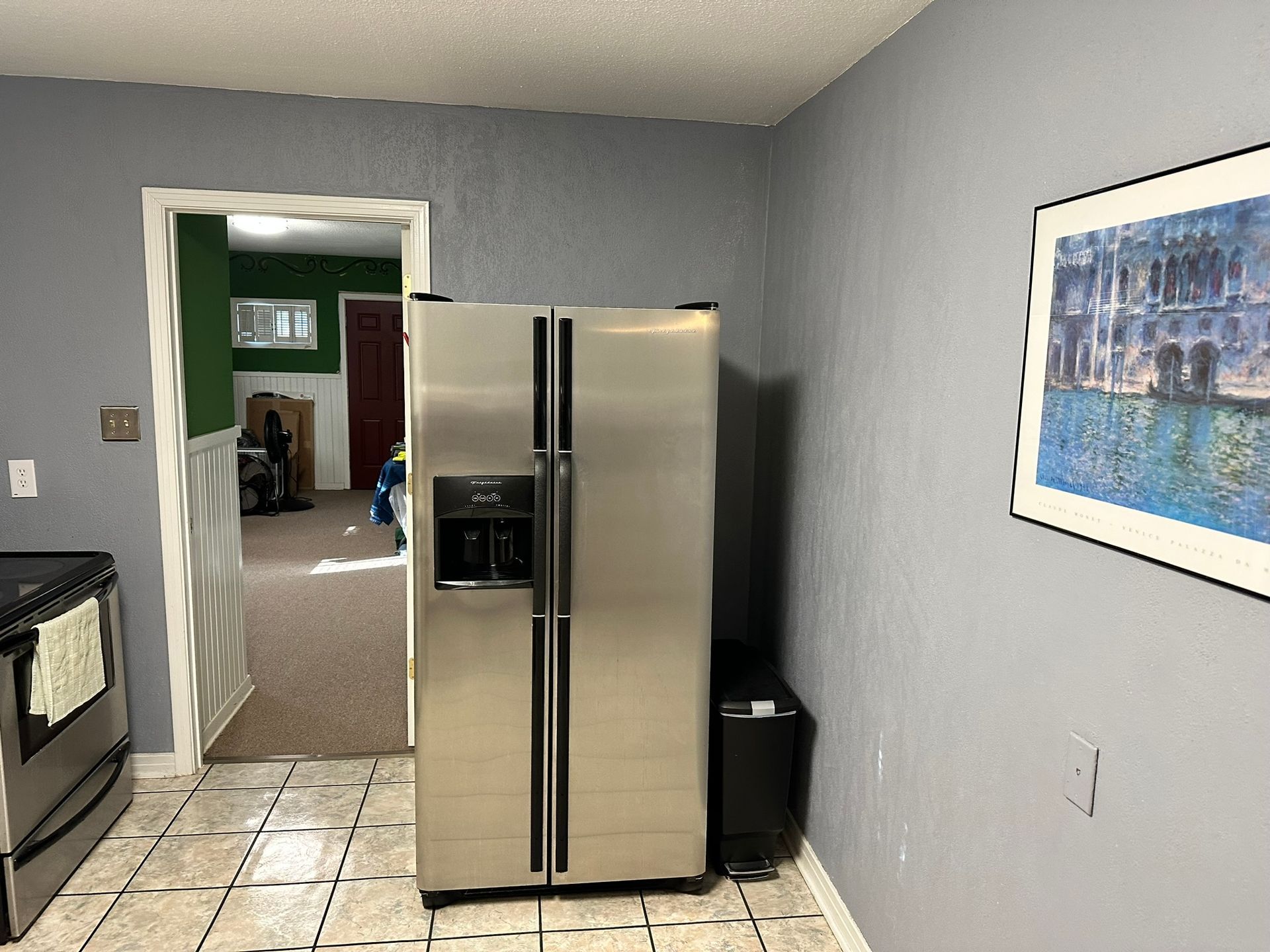 A kitchen with a stainless steel refrigerator and a picture on the wall.