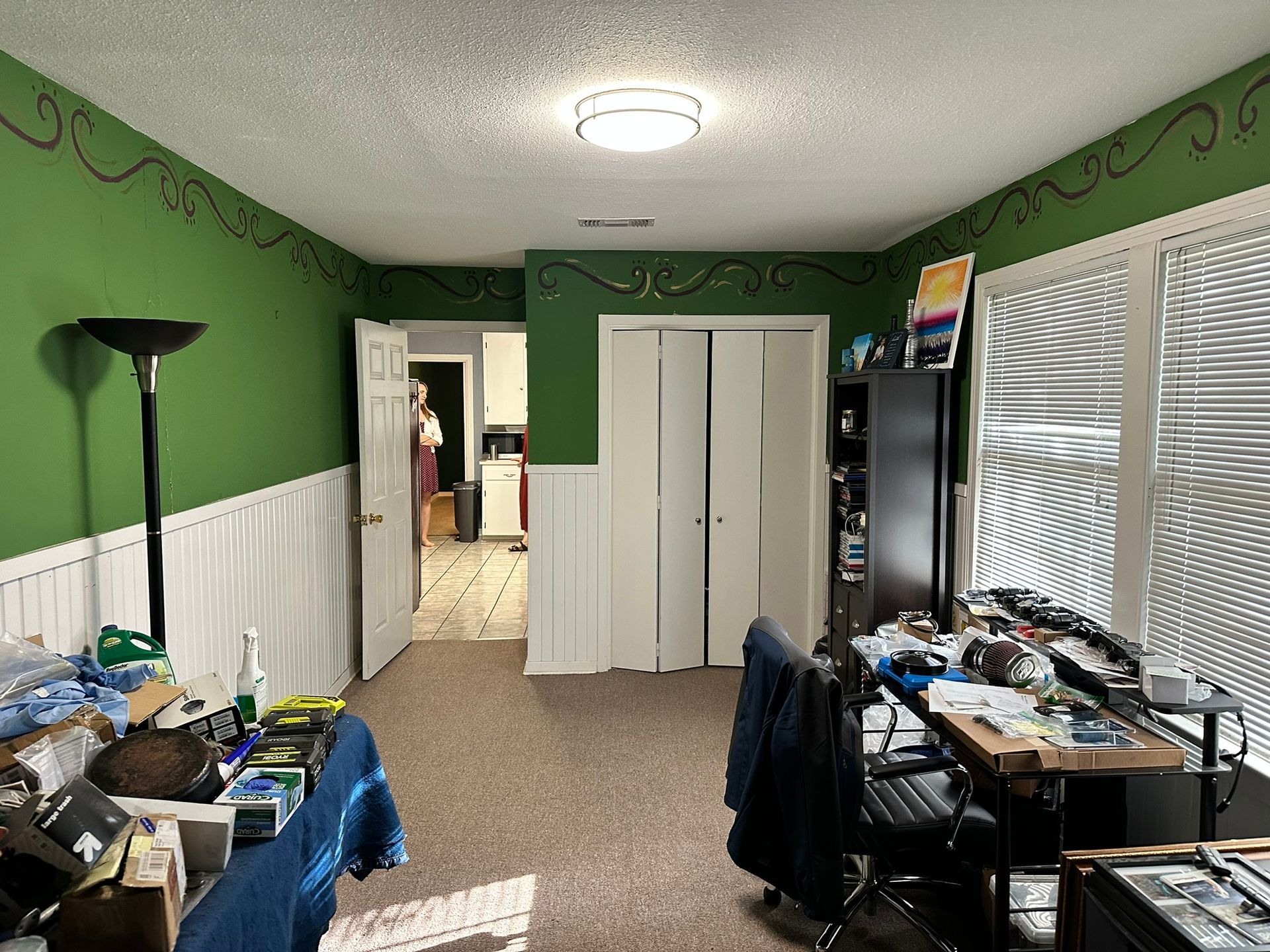 A room with green walls and white trim has a desk and chairs in it.