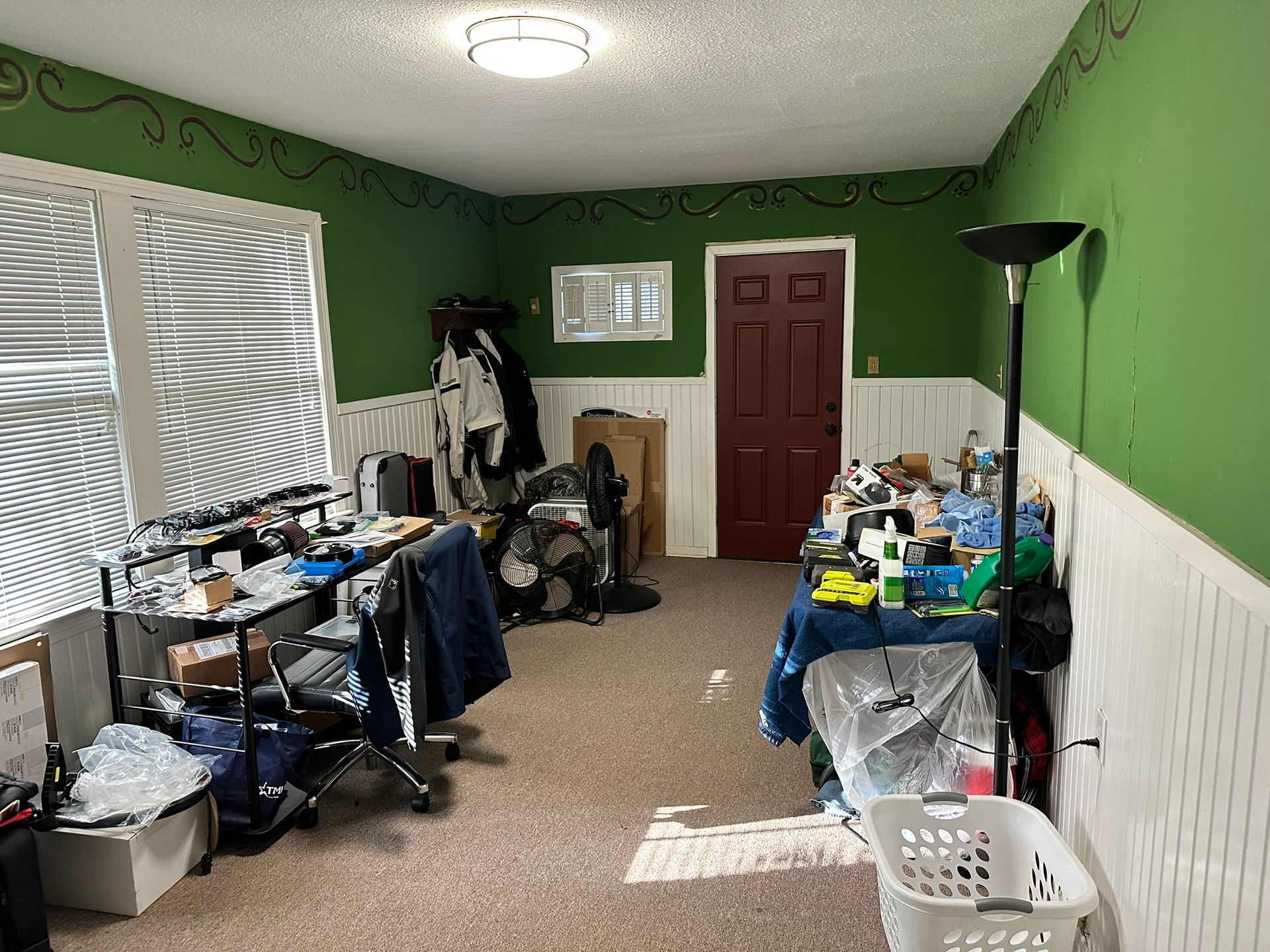 A room with green walls , white trim , and a laundry basket.