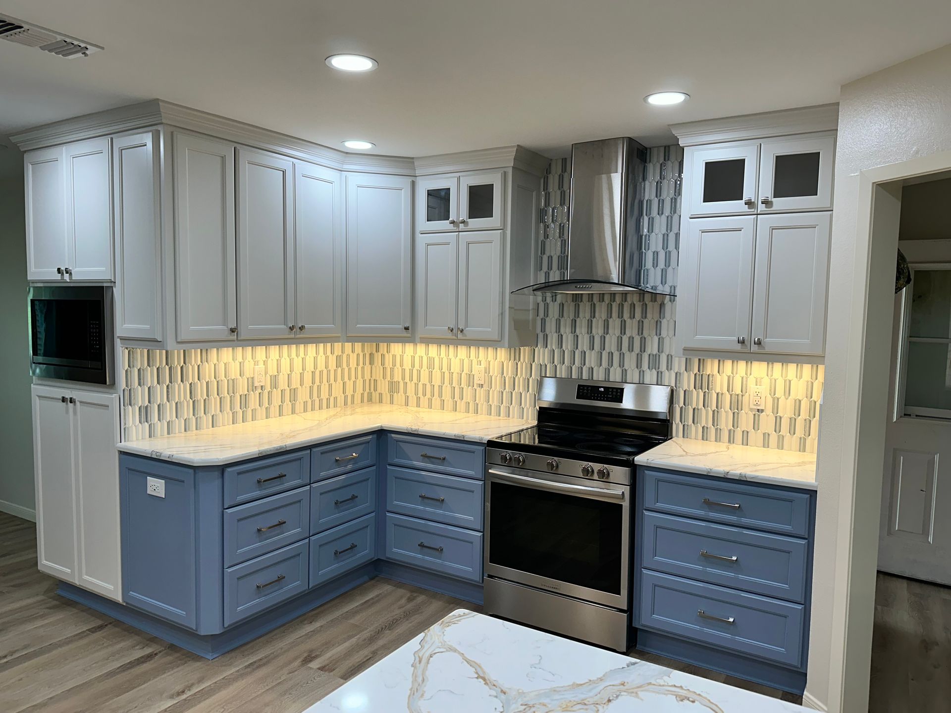 A kitchen with blue cabinets , white counter tops , stainless steel appliances and a stove.