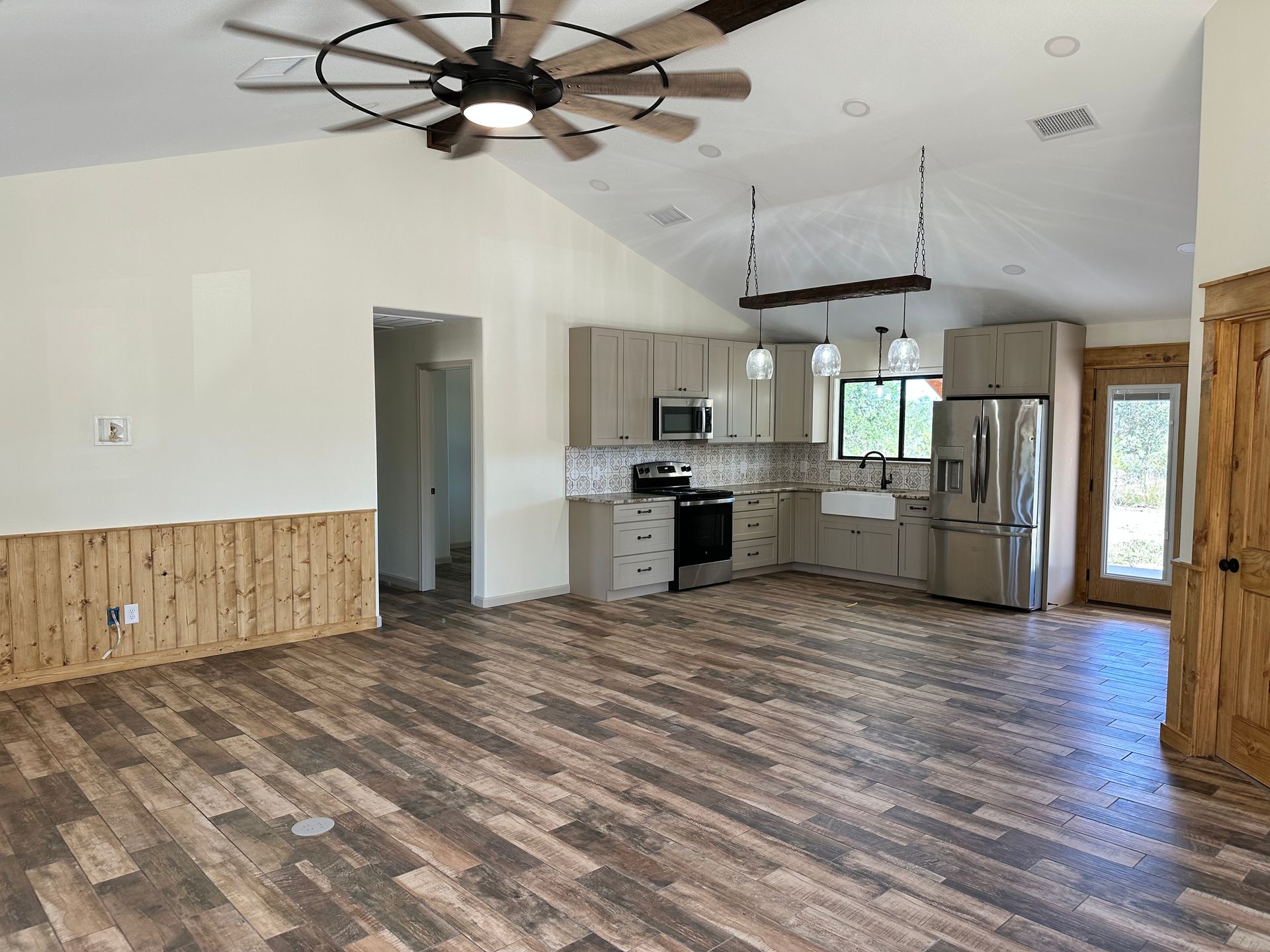 There is a ceiling fan in the living room and a kitchen in the background.