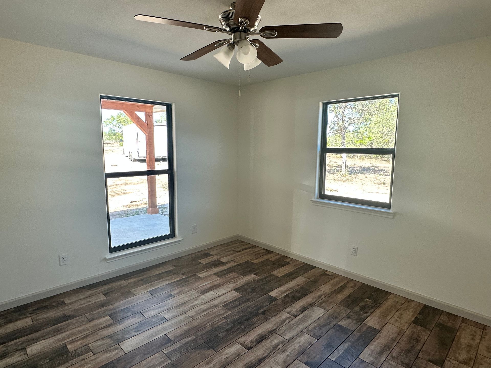 An empty room with a ceiling fan and two windows.