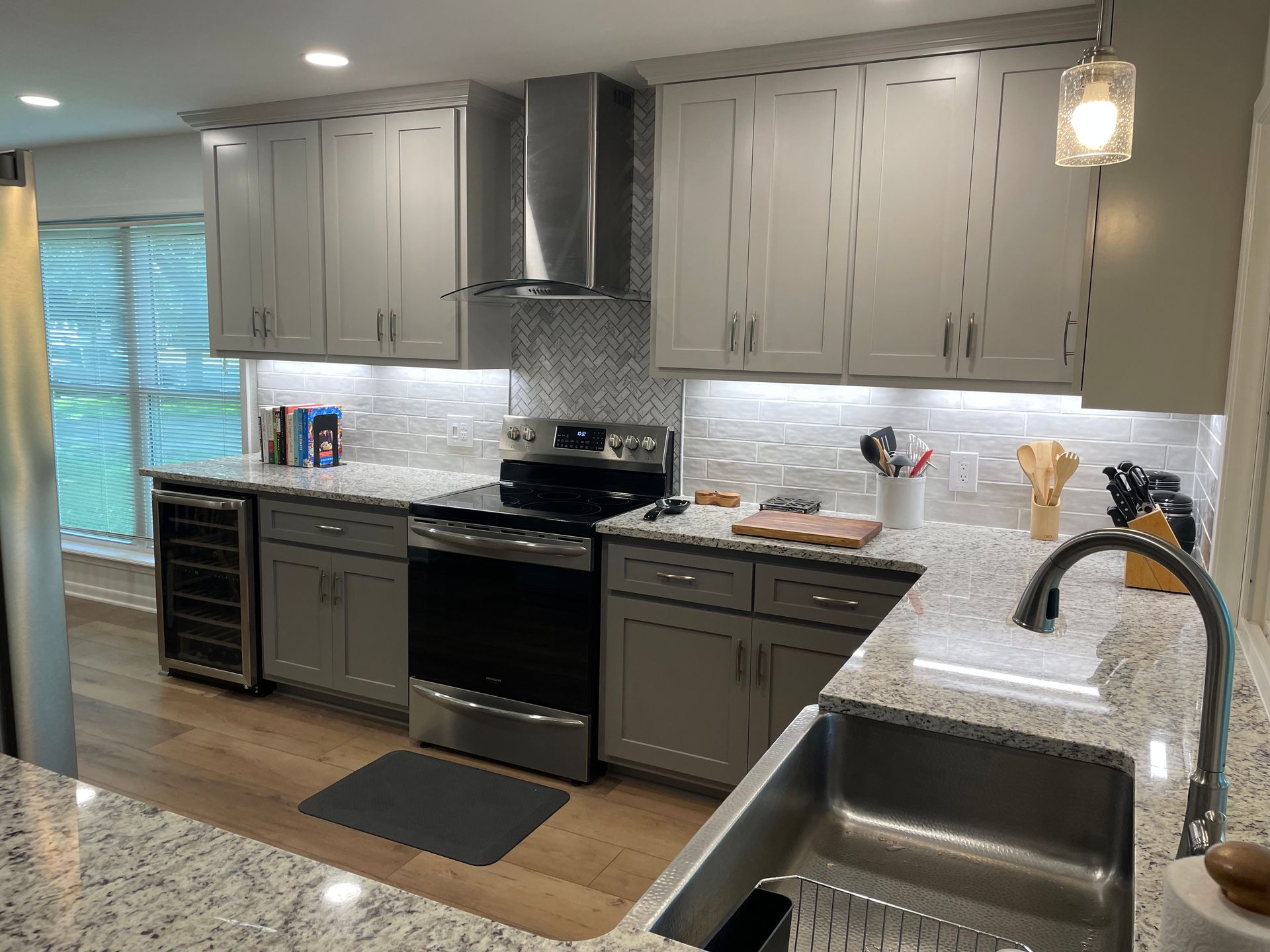 A kitchen with stainless steel appliances , gray cabinets , granite counter tops , and a sink.