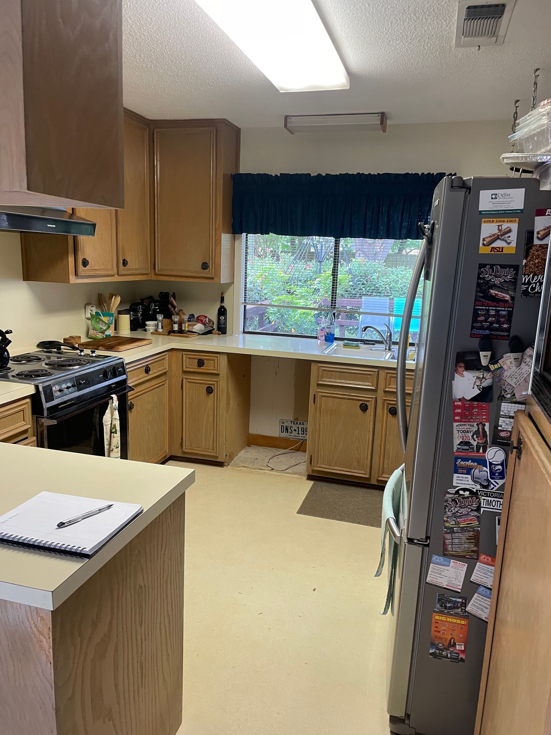 A kitchen with wooden cabinets , a stove , a refrigerator , and a window.