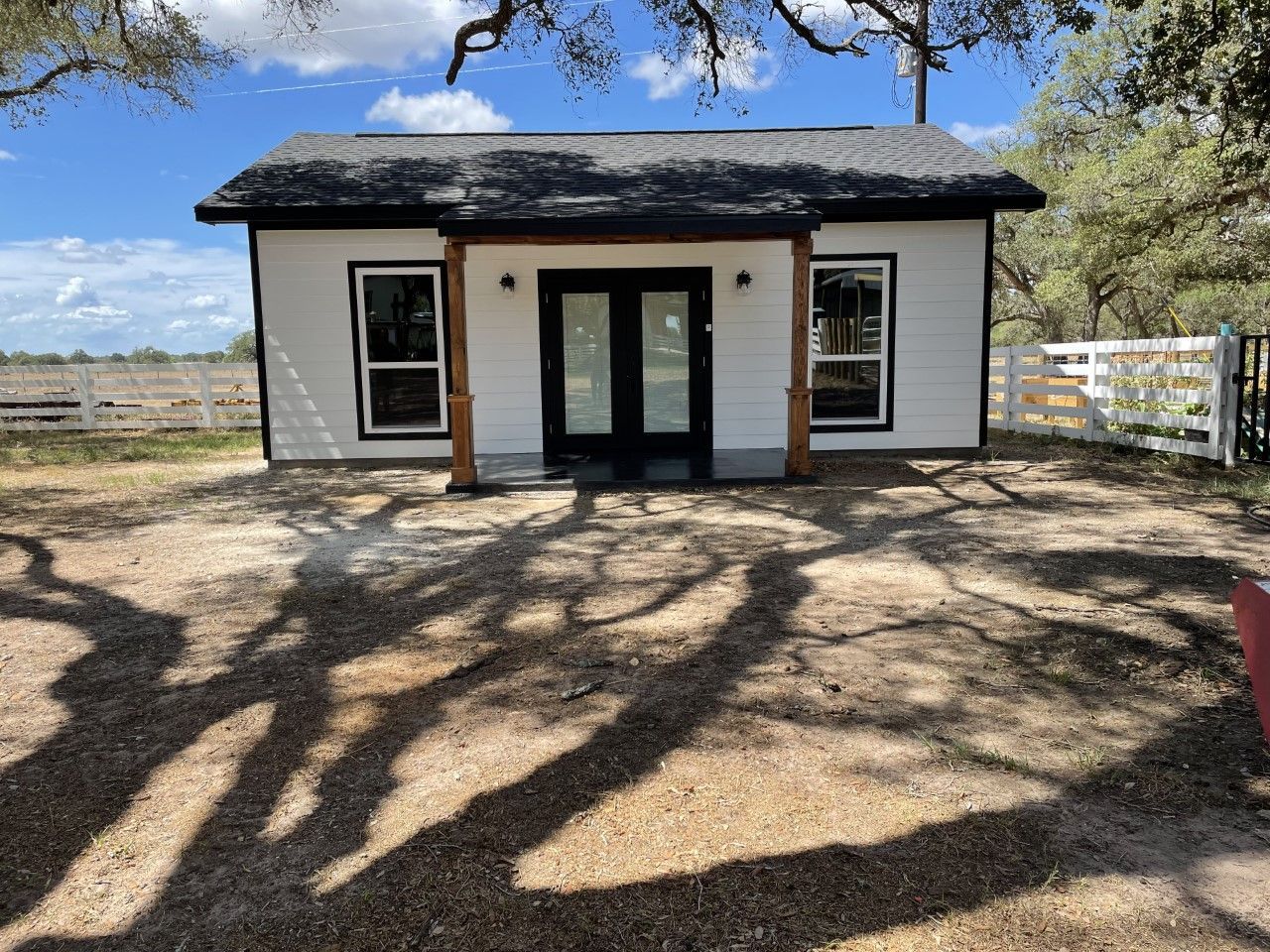 A small white house with a black roof is sitting in the middle of a dirt field.