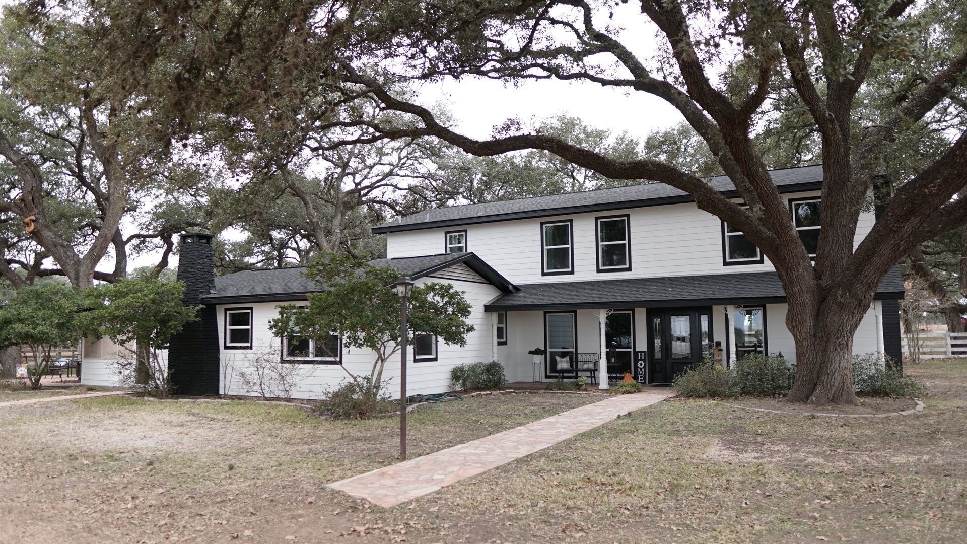 A large white house with a black roof is surrounded by trees.