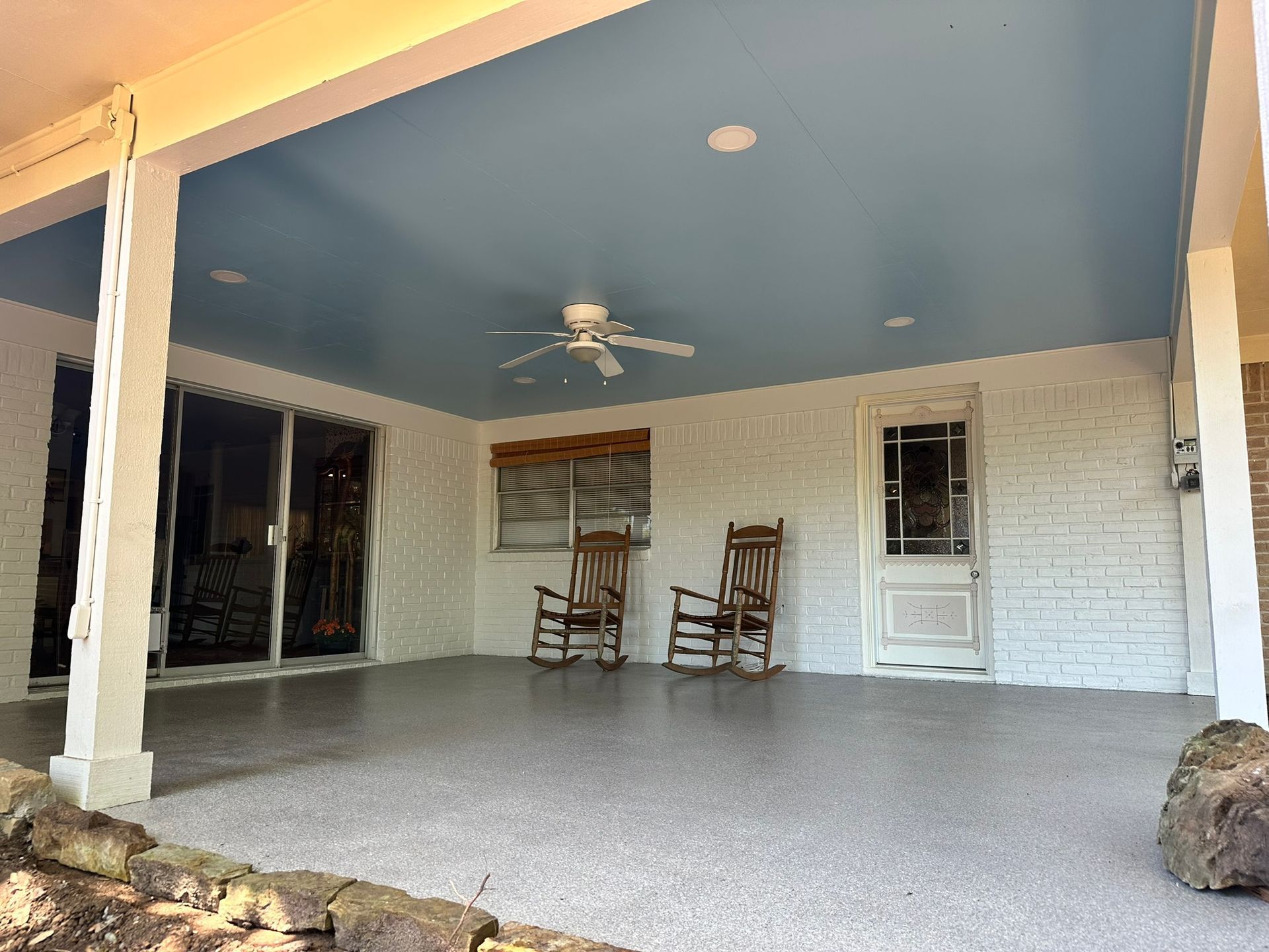 A porch with two rocking chairs and a ceiling fan.
