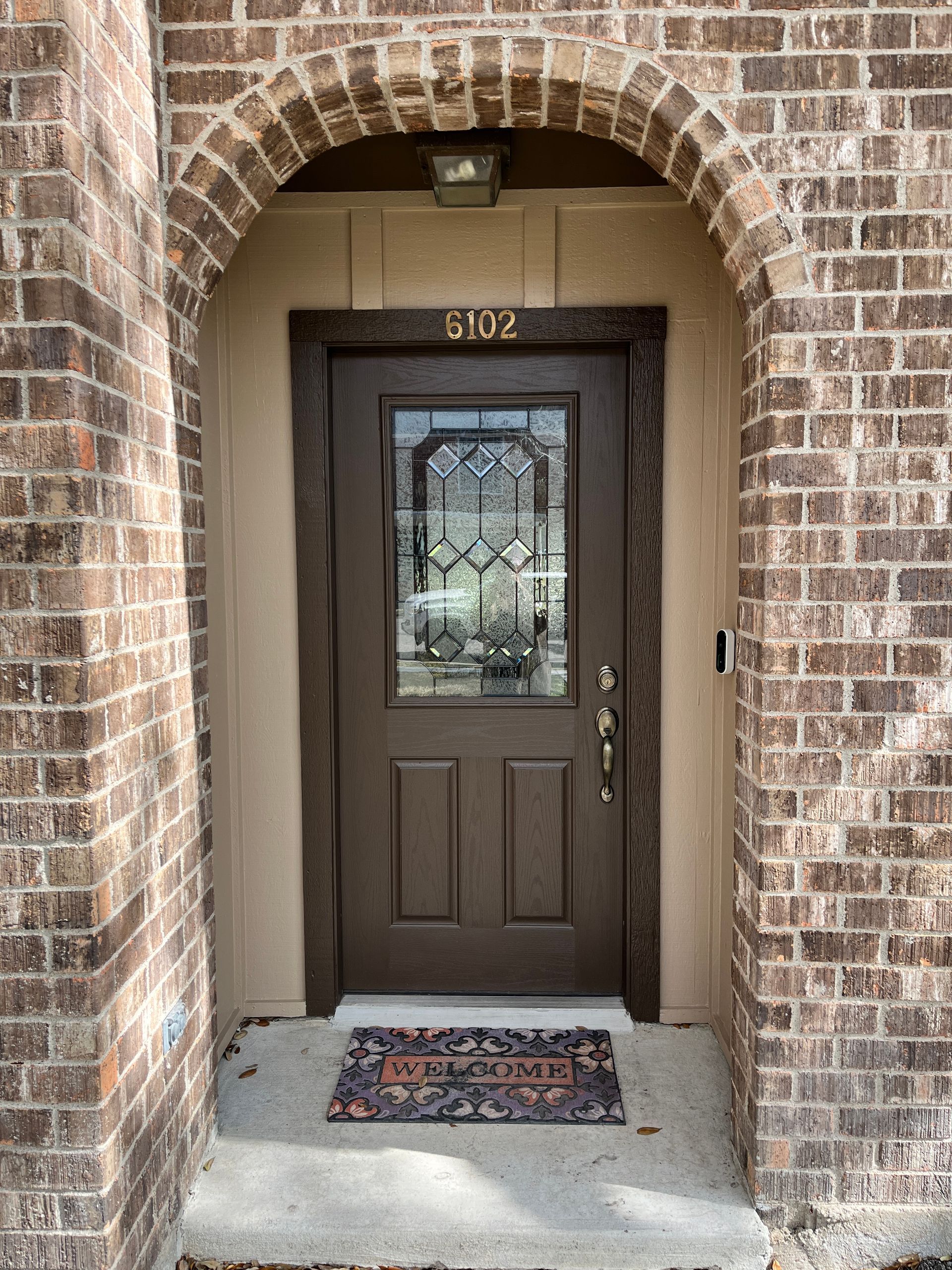 A brown door with a stained glass window is on a brick building.
