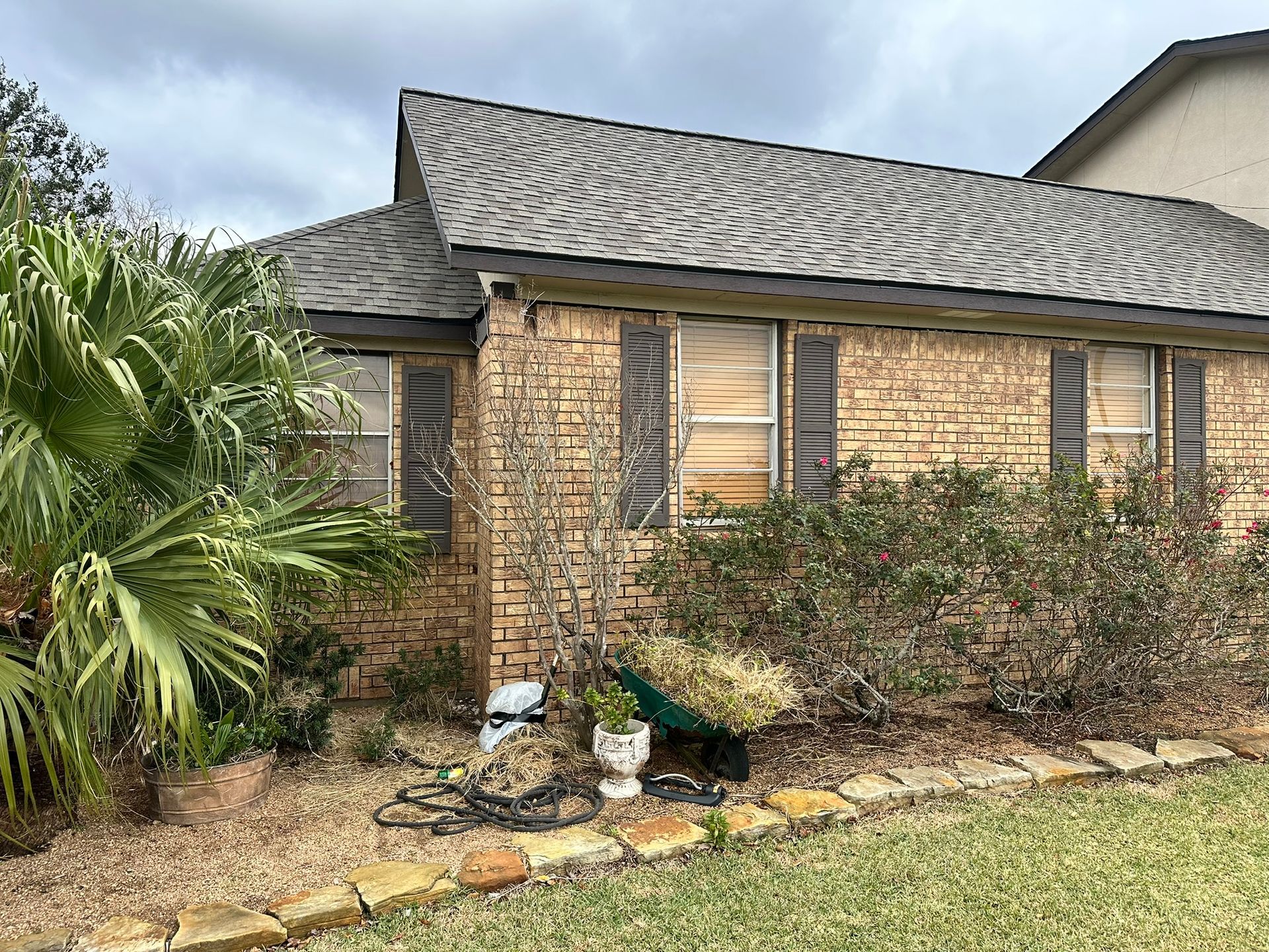 A brick house with shutters on the windows and a wheelbarrow in front of it.