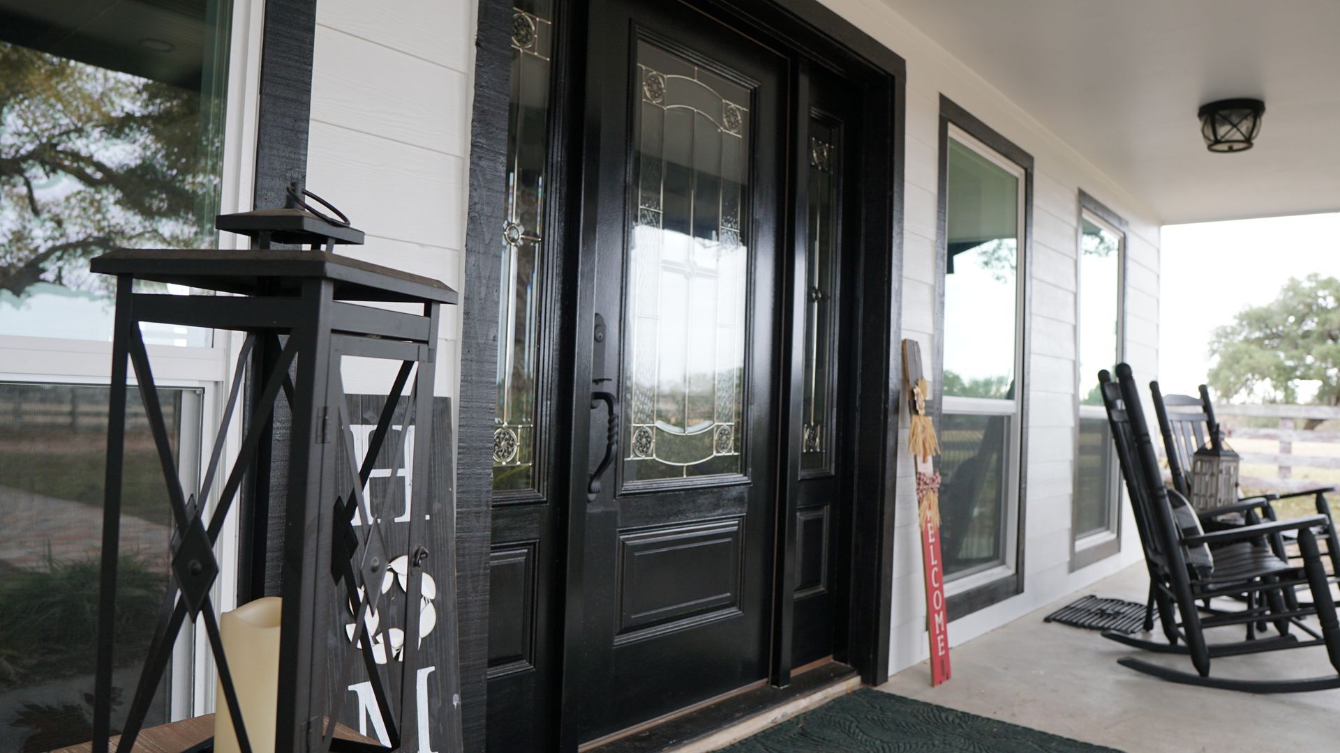 A black door is on a white house with rocking chairs on the porch.