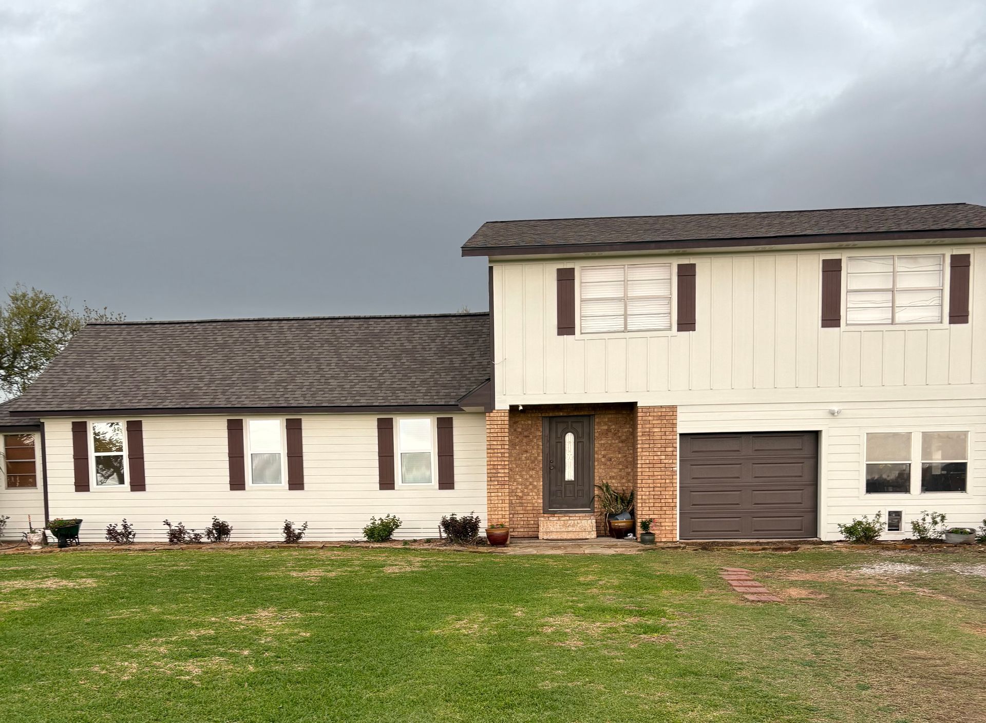 A large white house with a brown garage door is sitting on top of a lush green field.
