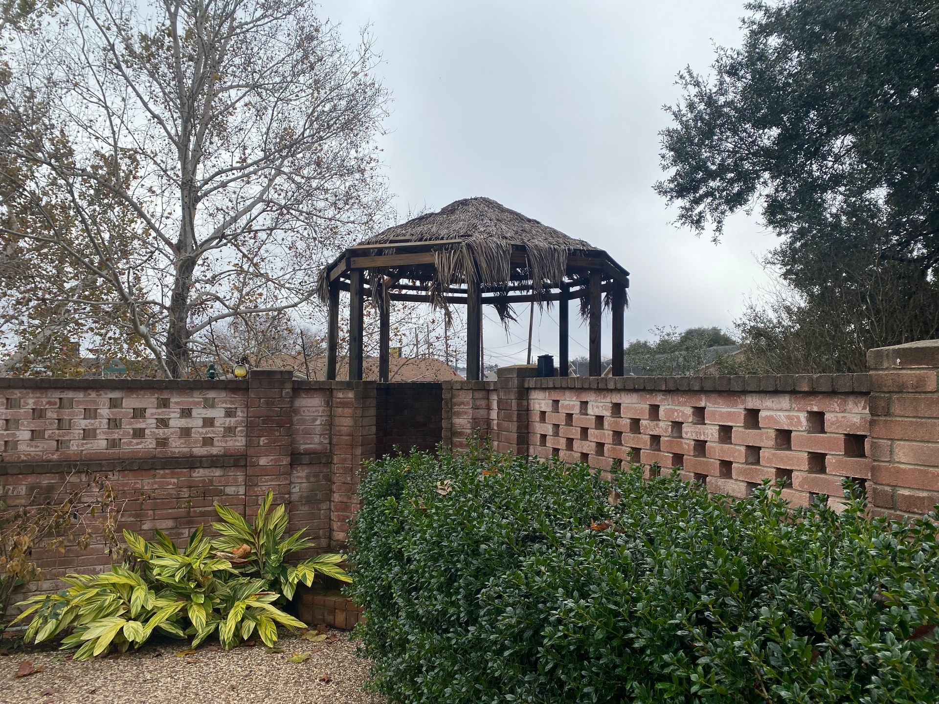 A gazebo with a thatched roof is behind a brick wall.