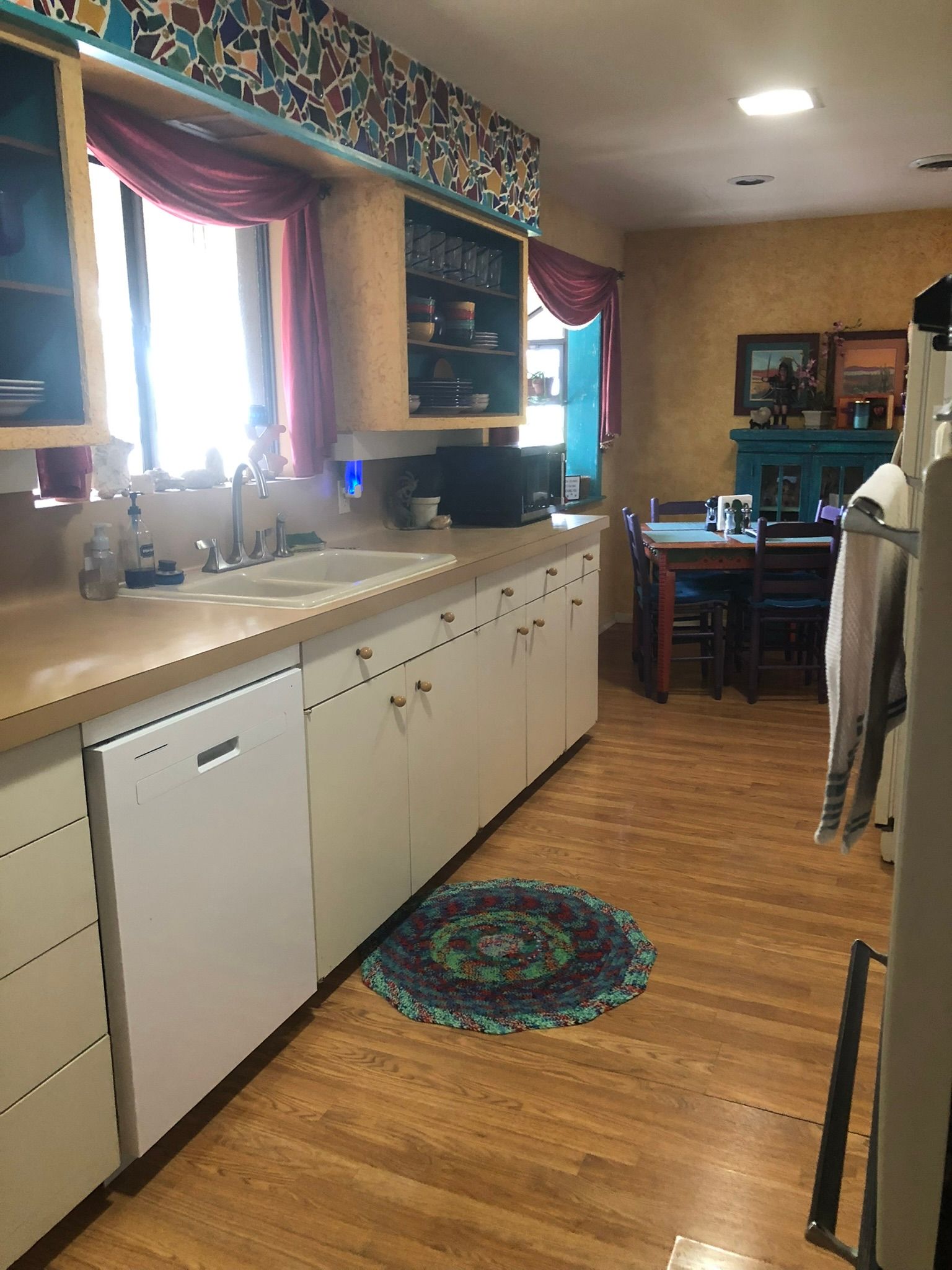 A kitchen with white cabinets , a dishwasher , a sink , and a rug on the floor.