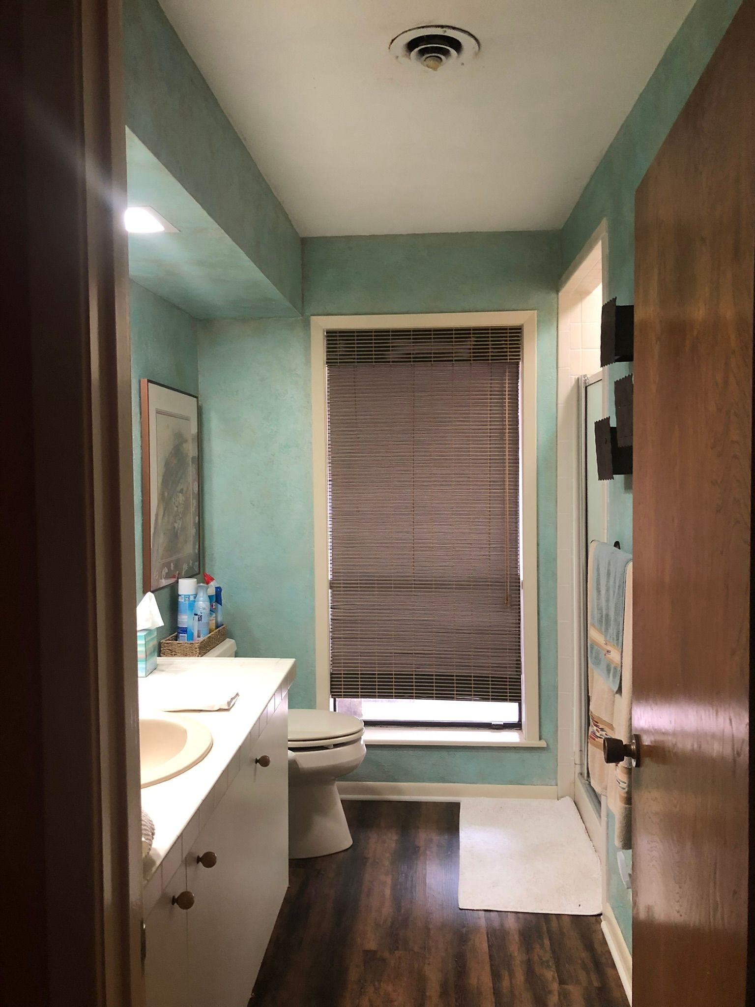 A bathroom with a toilet , sink , mirror and window.