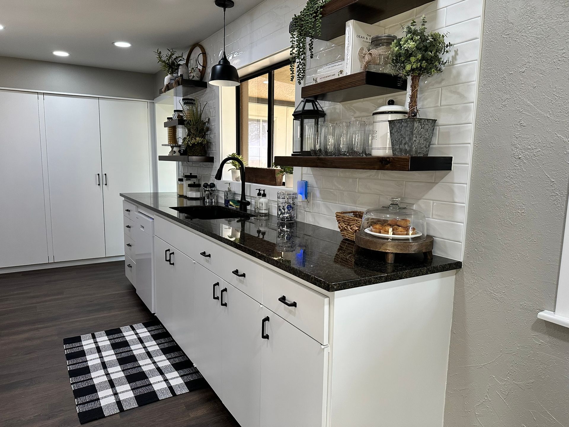 A kitchen with white cabinets , black counter tops , and a black and white checkered rug.