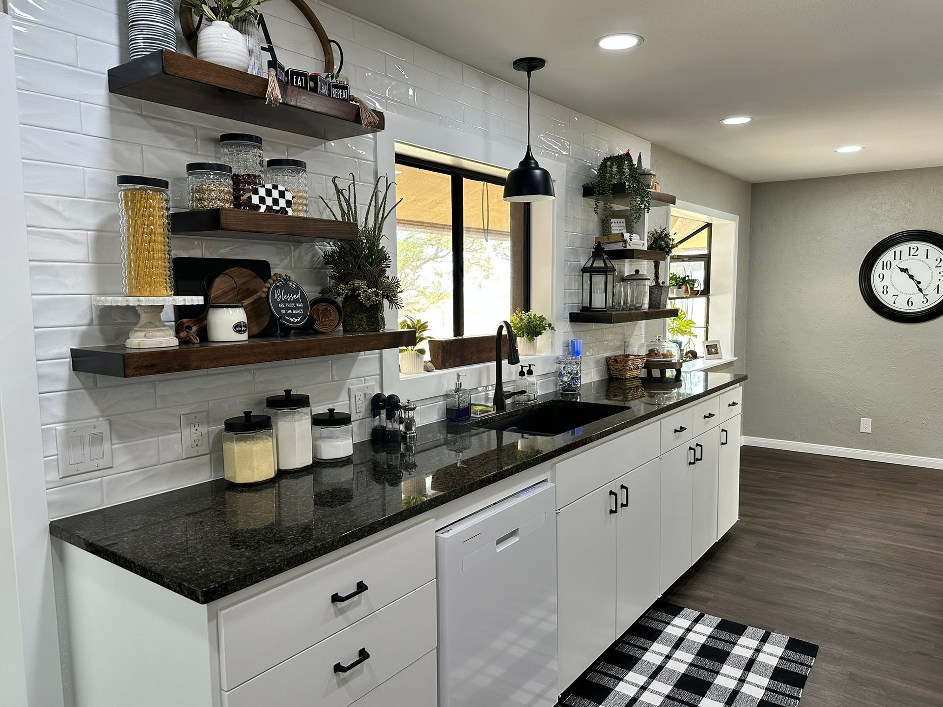 A kitchen with white cabinets , black counter tops , a sink , and a clock on the wall.