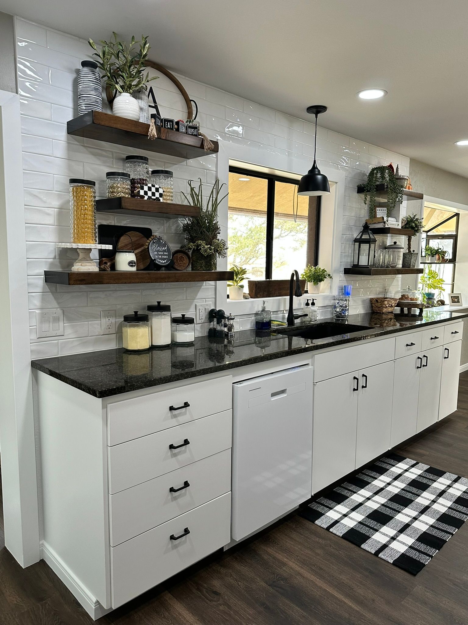 A kitchen with white cabinets , black counter tops , and a black and white checkered rug.