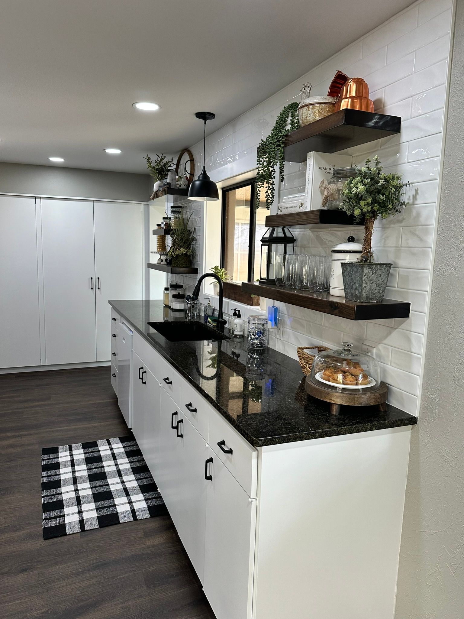 A kitchen with white cabinets , black counter tops , and a black and white checkered rug.