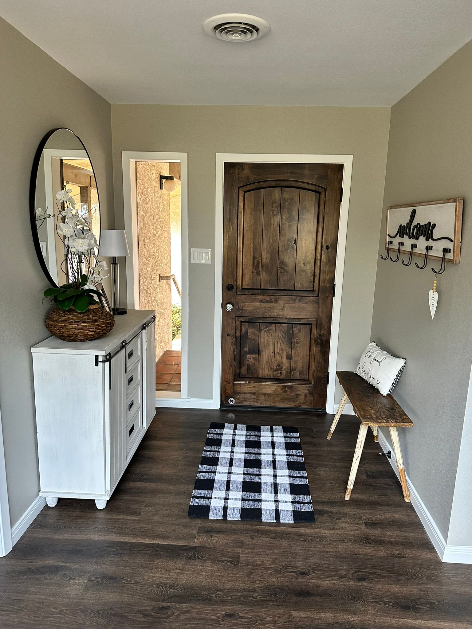 A hallway with a wooden door , a bench , a mirror and a rug.