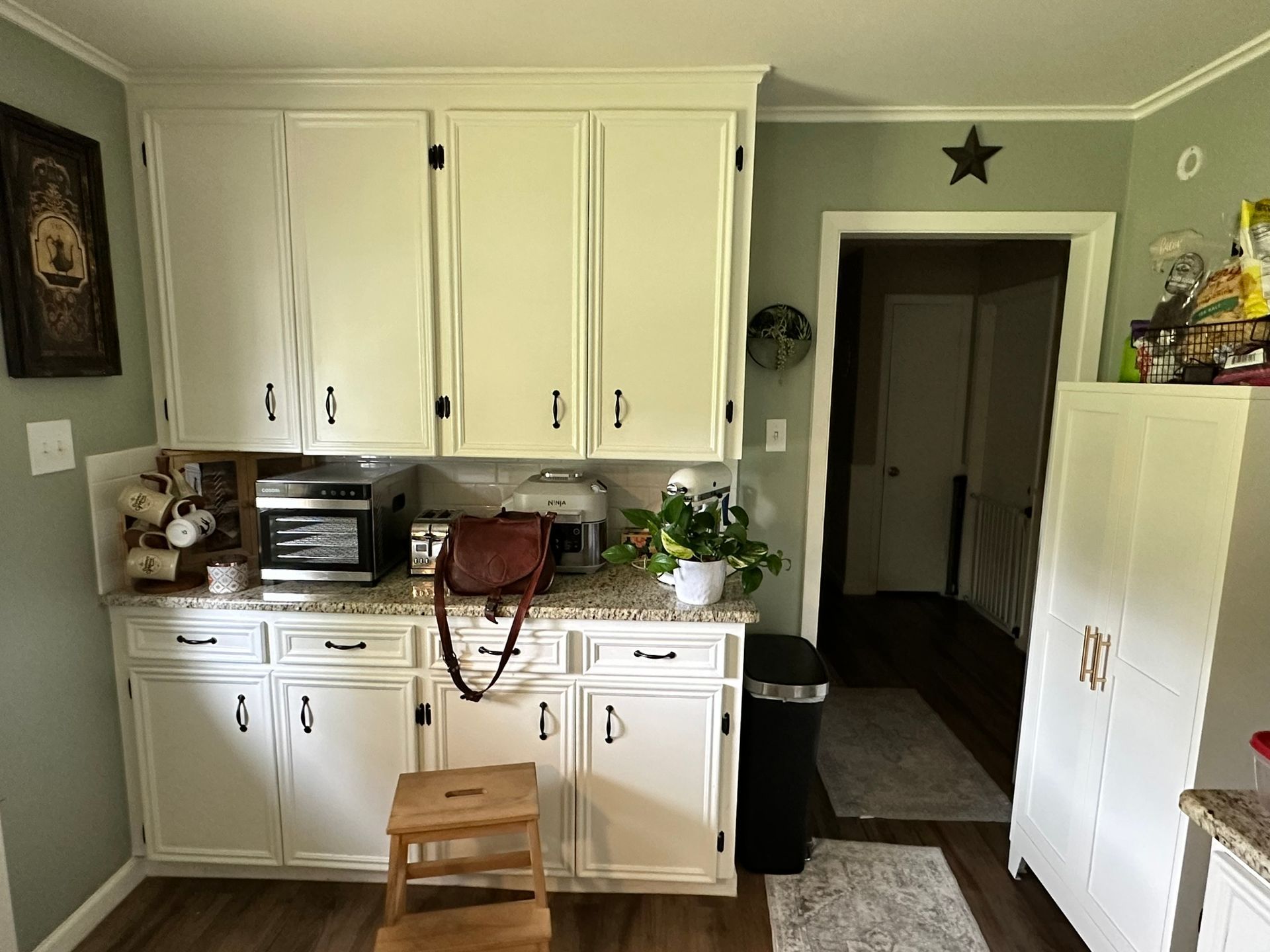 A kitchen with white cabinets , granite counter tops , a microwave , and a stool.