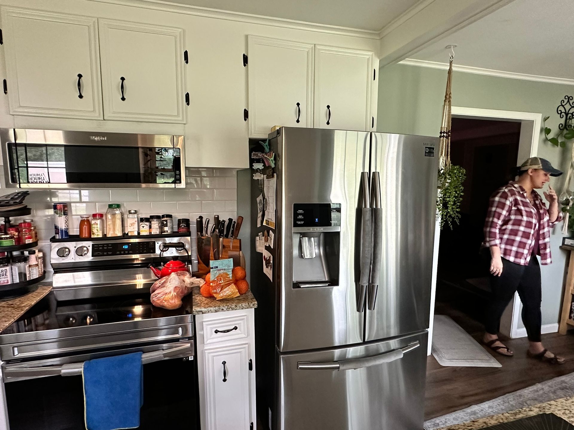 A woman is standing in a kitchen next to a stainless steel refrigerator.