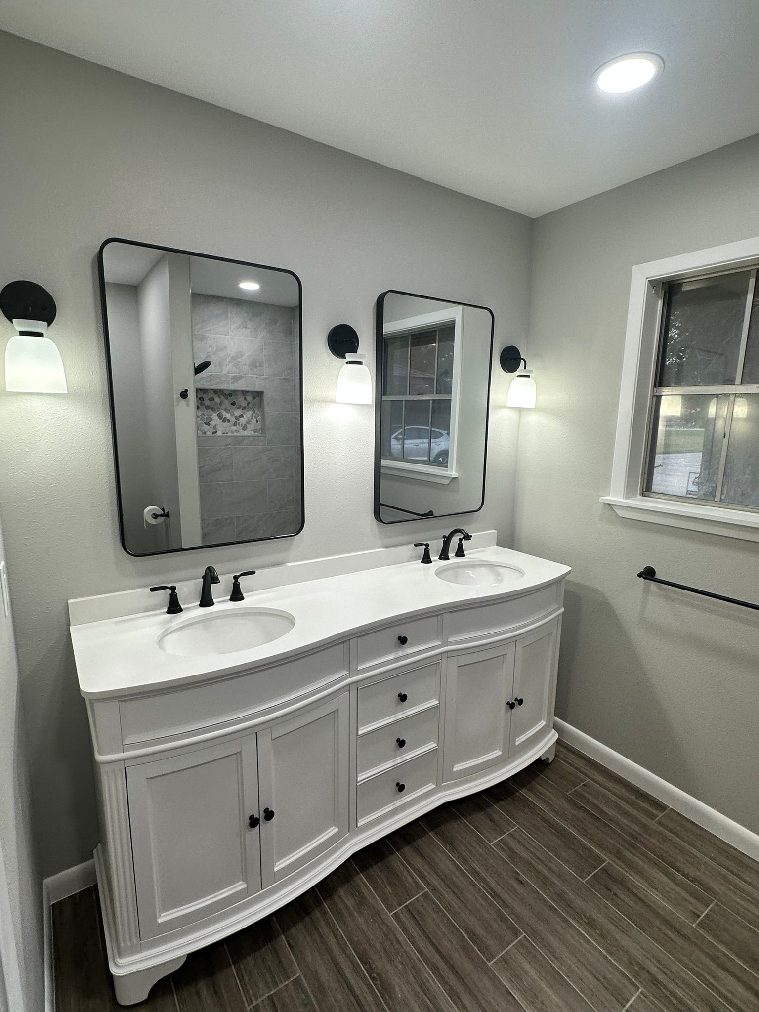 A bathroom with two sinks , two mirrors and a window.