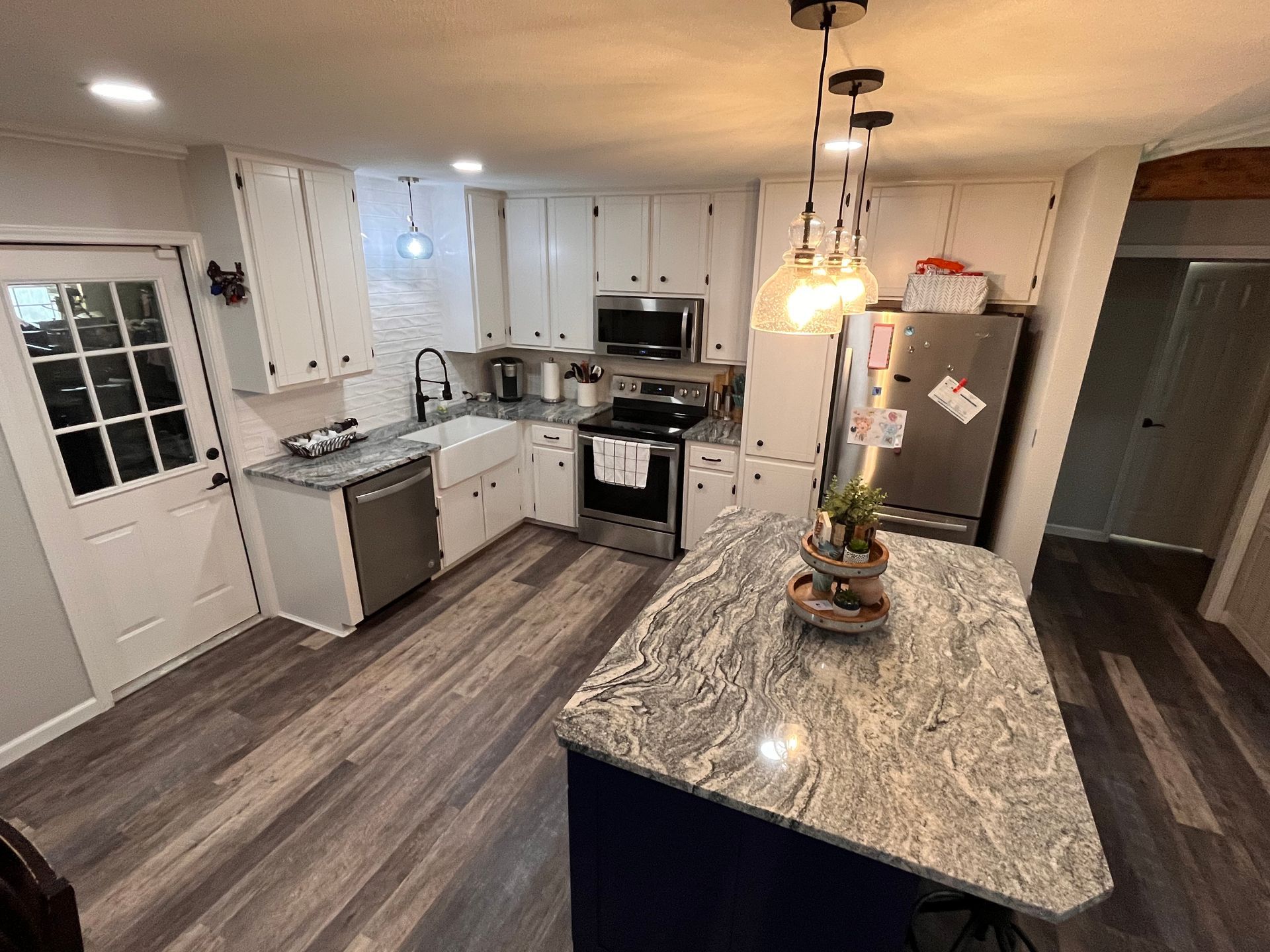 A kitchen with white cabinets , granite counter tops , stainless steel appliances and a large island.