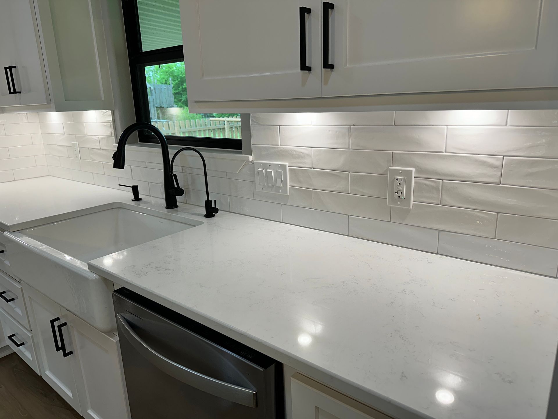 A kitchen with white cabinets , a sink , and a stainless steel dishwasher.