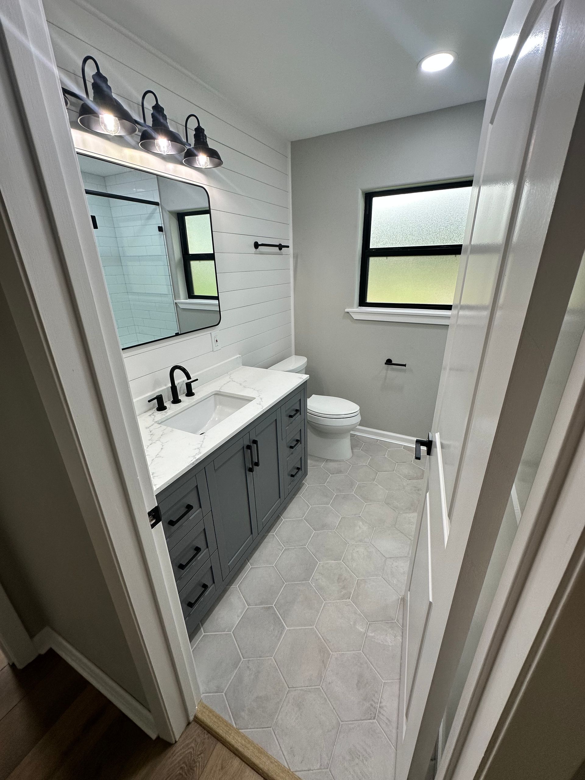 A bathroom with a sink , toilet , mirror and window.