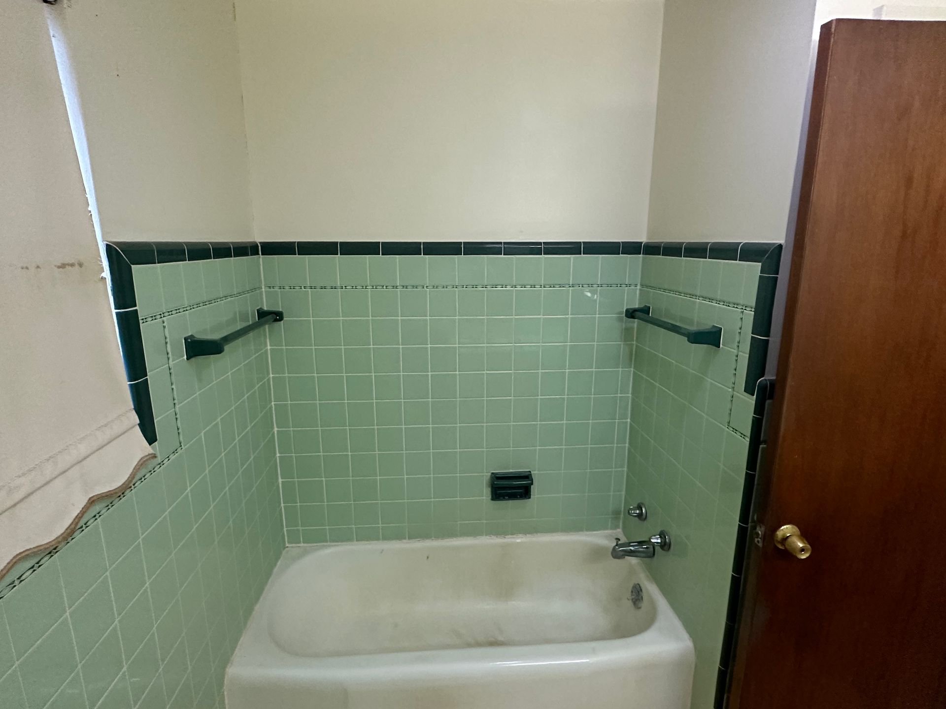 A bathroom with green tiles and a bathtub