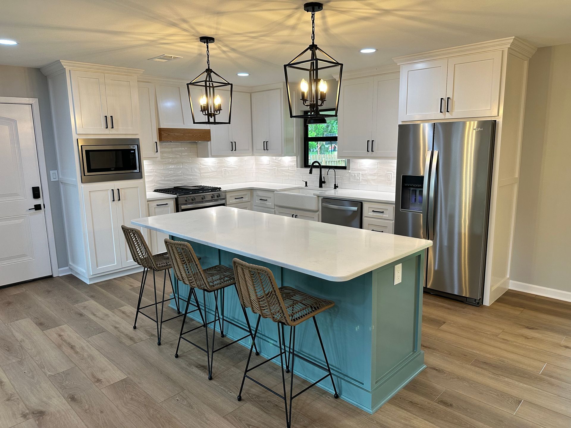 A kitchen with white cabinets , stainless steel appliances , a large island and stools.