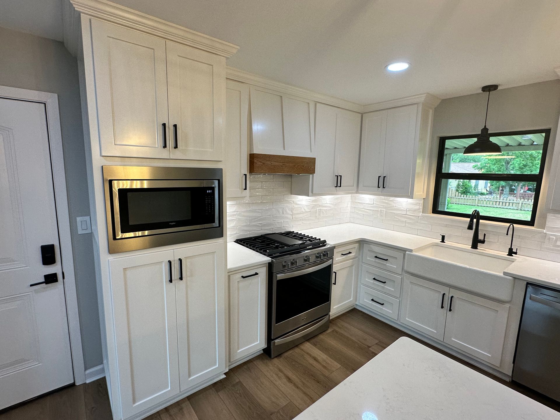 A kitchen with white cabinets , a stove , a microwave , a sink , and a window.