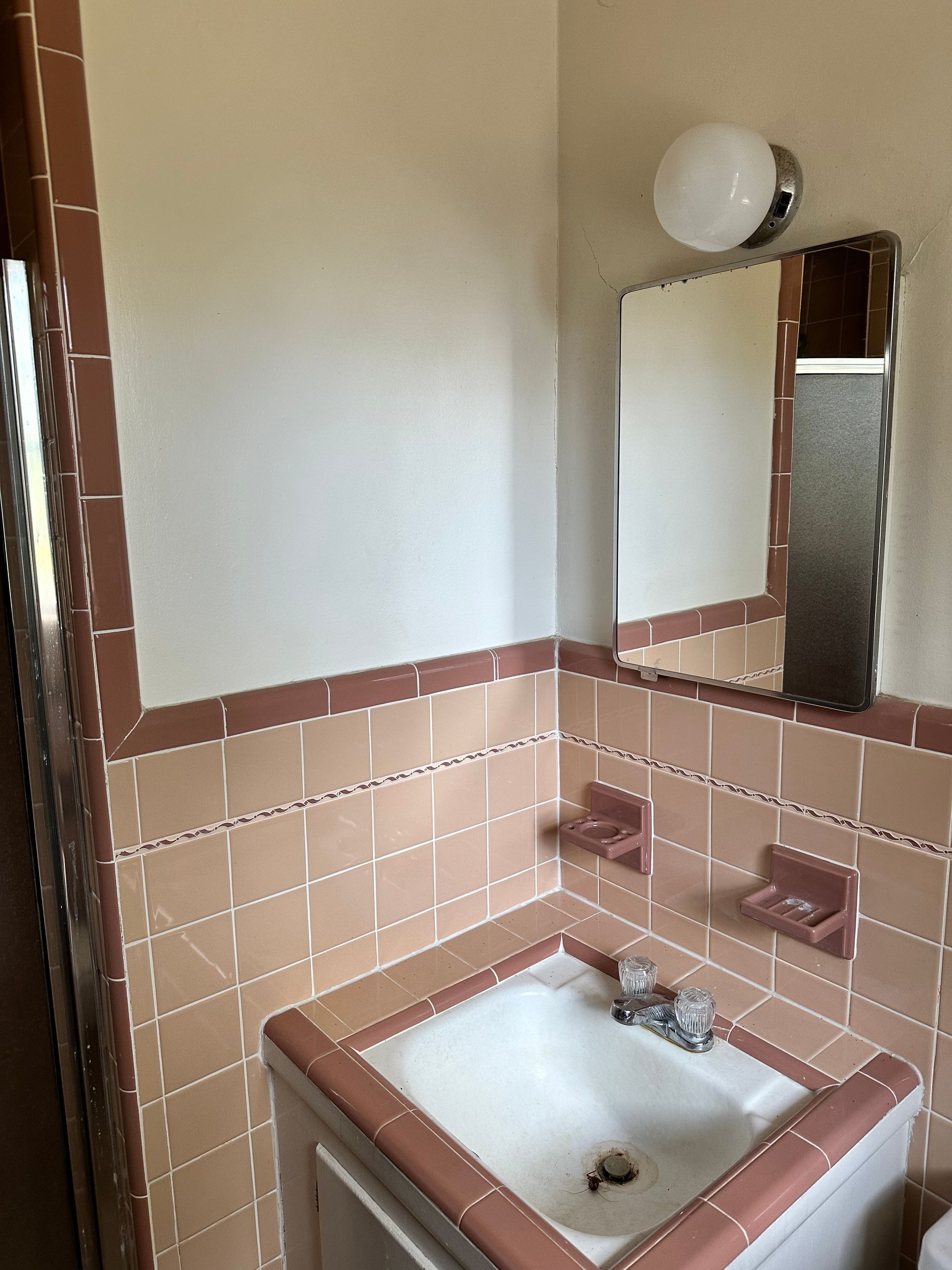 A bathroom with pink tiles and a sink and mirror