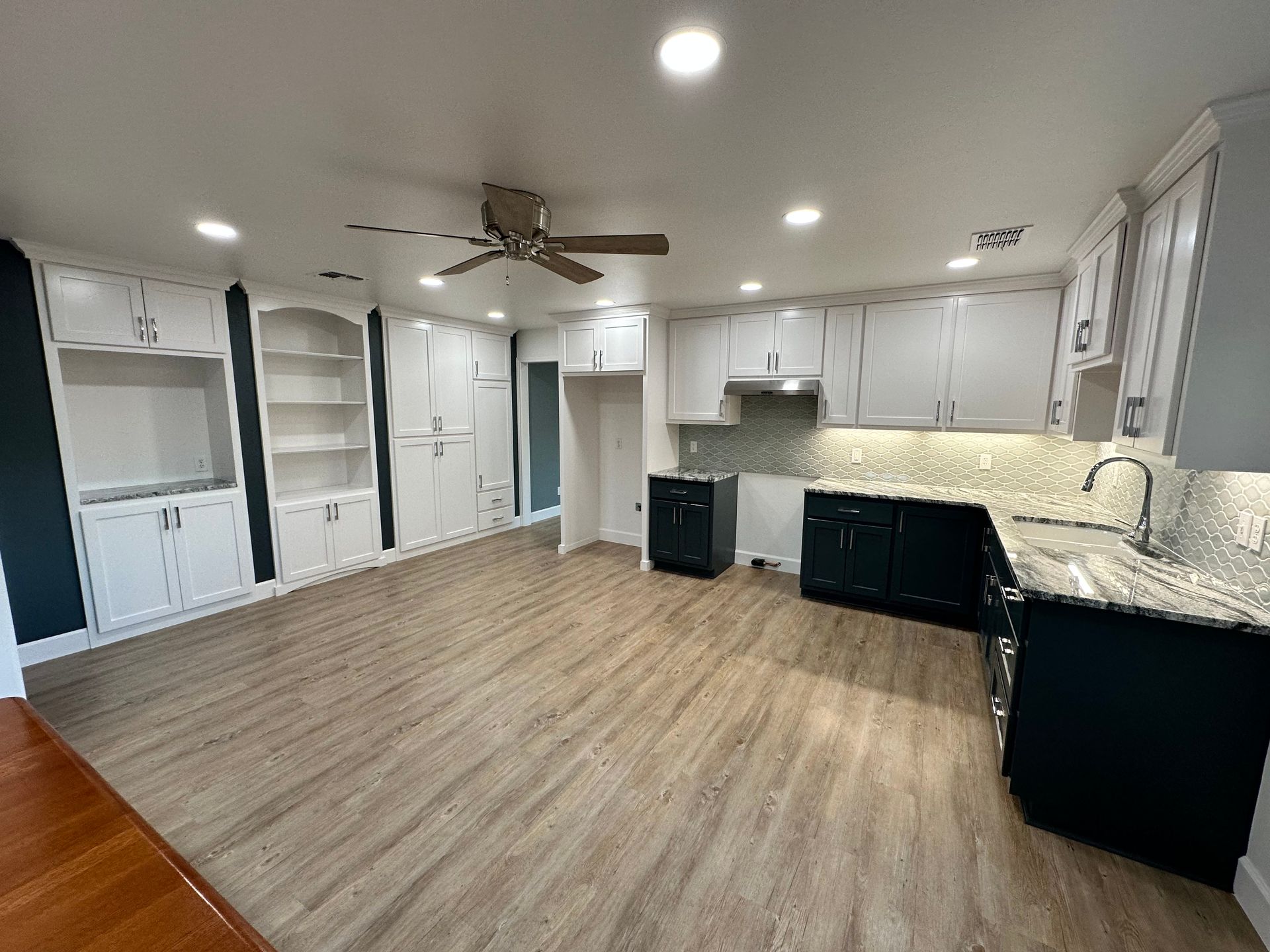 A kitchen with white cabinets , black counter tops , and a ceiling fan.