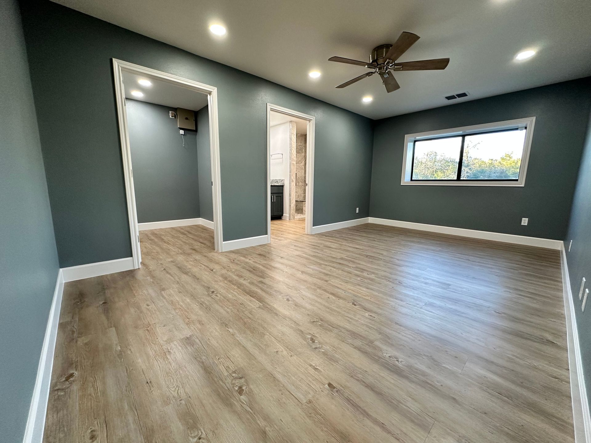An empty living room with a ceiling fan and a window.