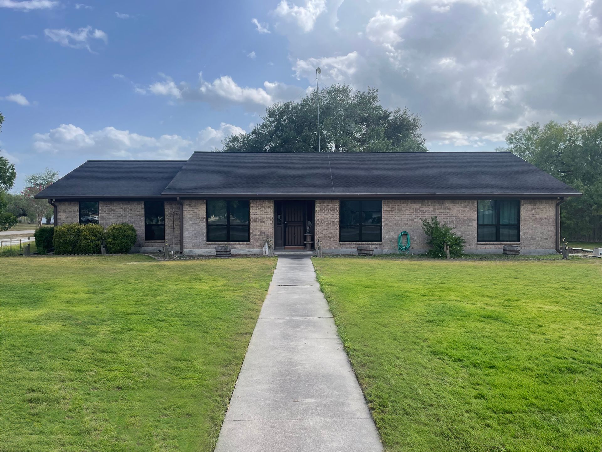 A brick house with a black roof and a concrete walkway leading to it.
