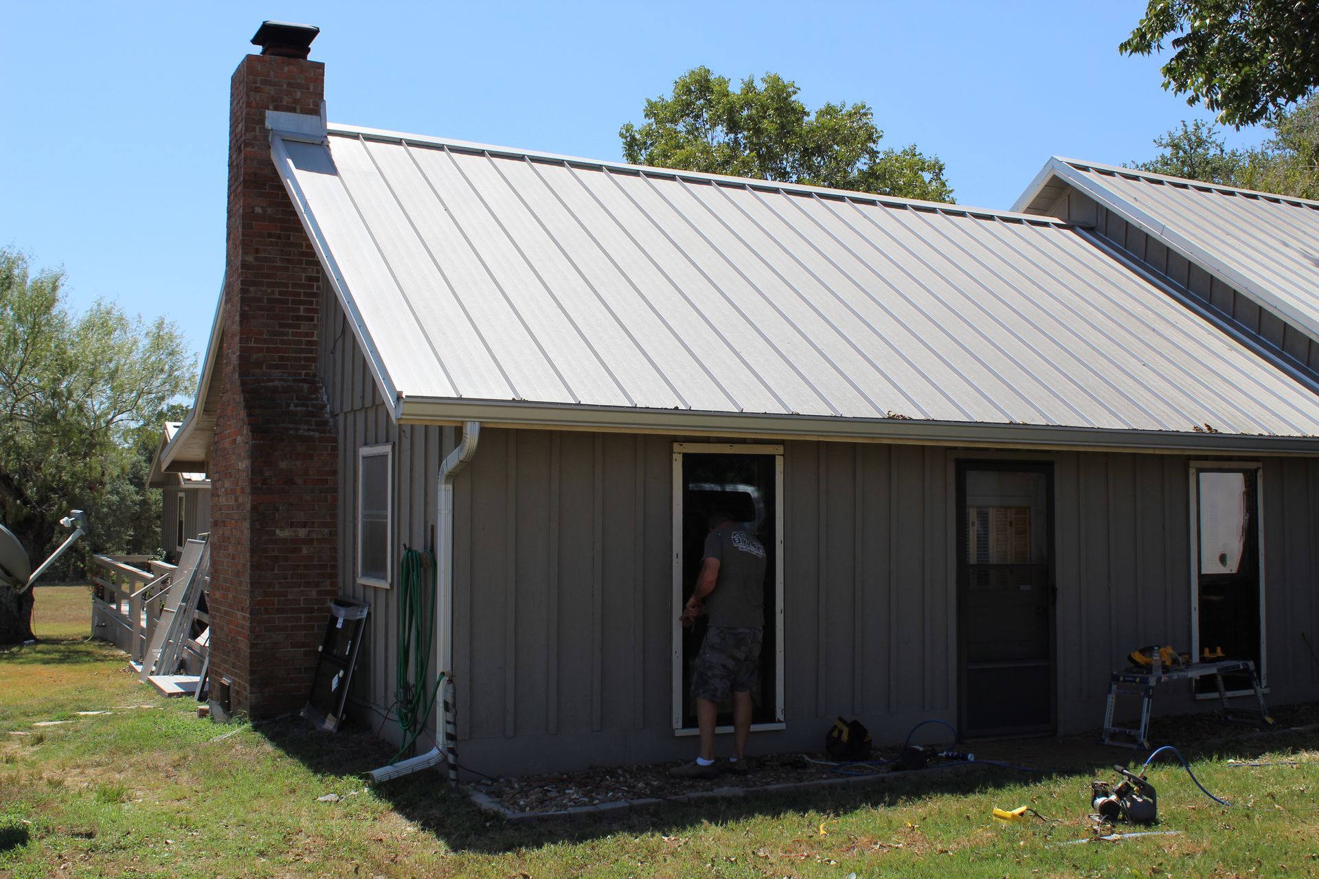 A man is standing in front of a house with a metal roof