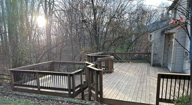 A large wooden deck is surrounded by trees and a house.