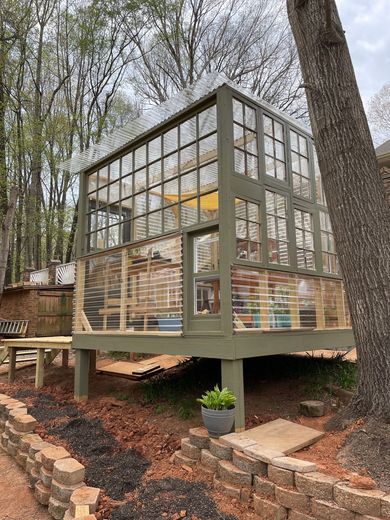 A greenhouse made out of old windows in the middle of a forest.