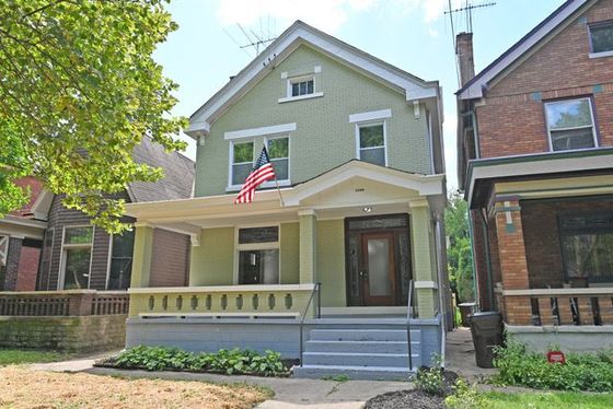A green house with an american flag on the front porch