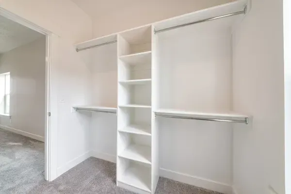 A walk in closet in a bedroom with shelves and hanging clothes.