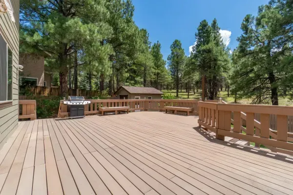 A large wooden deck with a grill and trees in the background.