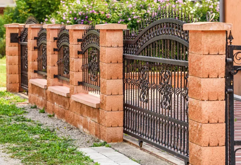 A brick fence with a wrought iron gate in front of a house.