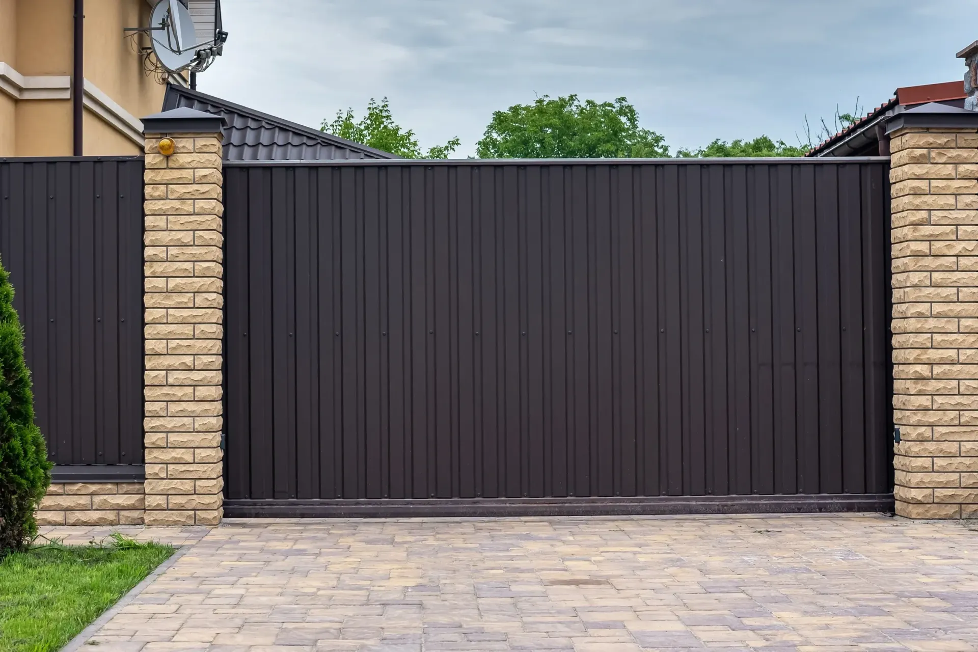 A black sliding gate with a brick fence in front of a house.