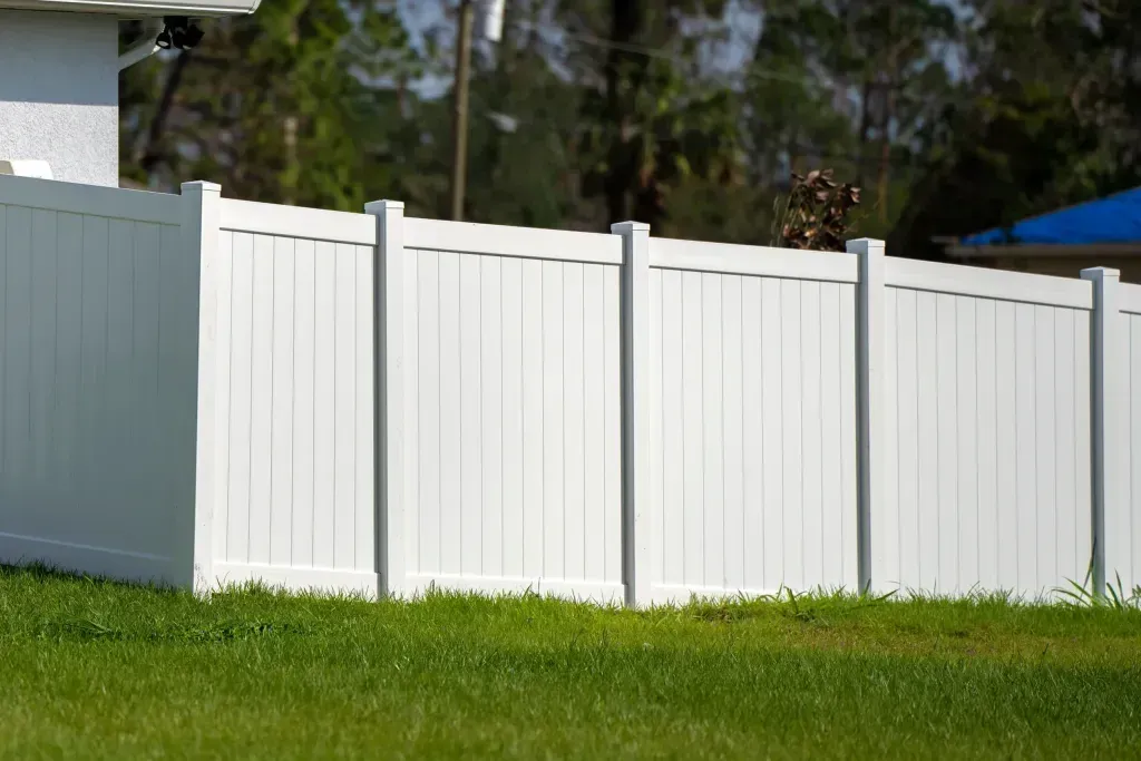 A white vinyl fence surrounds a lush green lawn in front of a house.