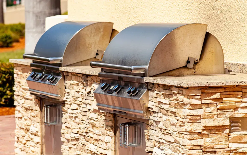 Two stainless steel grills are sitting on top of a stone wall.