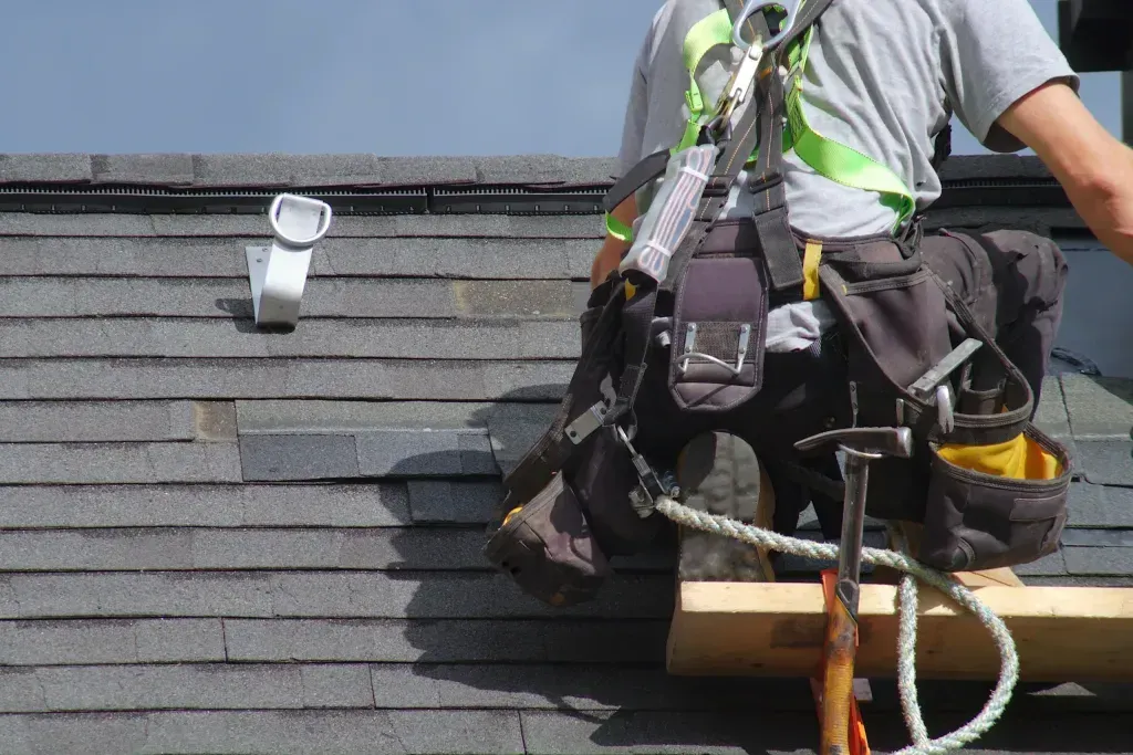 A man is sitting on top of a wooden plank on a roof.
