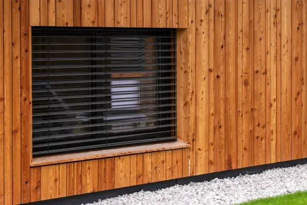 A wooden building with a window and blinds on it.