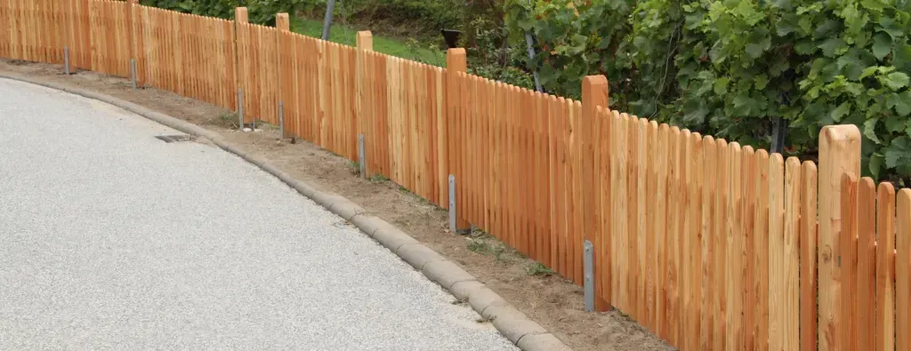 A wooden fence is along the side of a road.